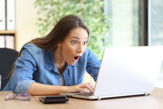 Kvinna som sitter och arbetar med sin laptop och ser väldigt förvånad ut.